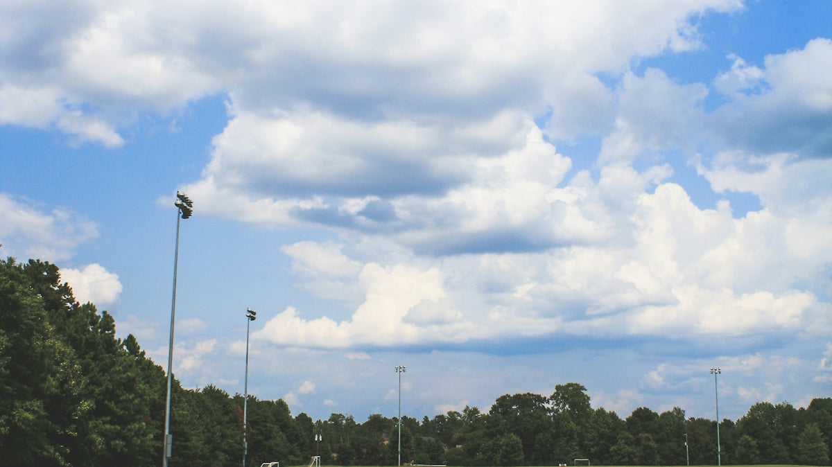 green soccer field surrounded with tall and green trees under white and blue sky during daytime