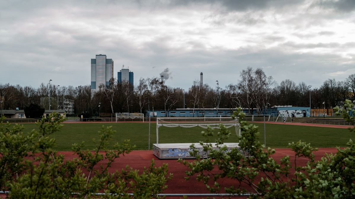 green grass field near city buildings under white clouds during daytime