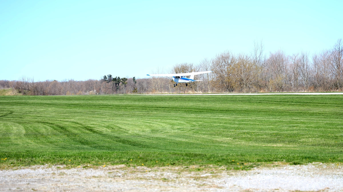 white and blue airplane flying over green grass field during daytime
