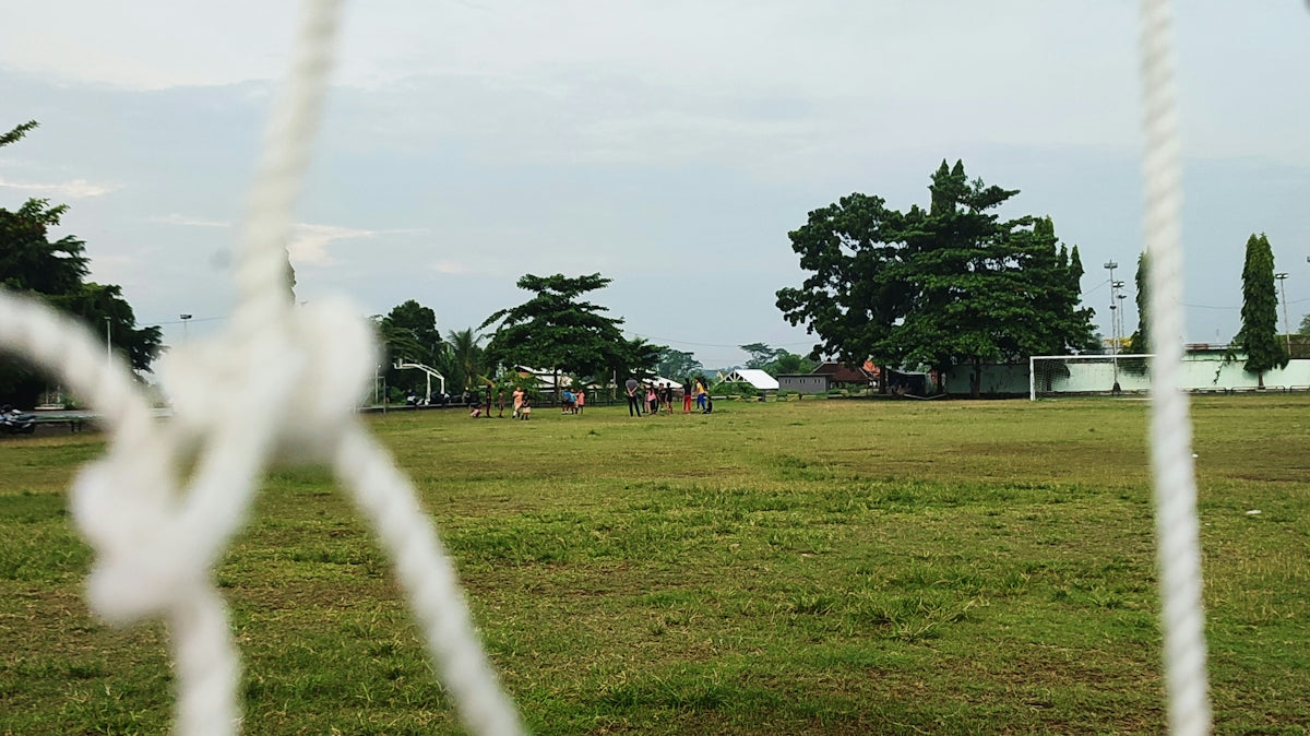 A close up of a soccer goal net with trees in the background