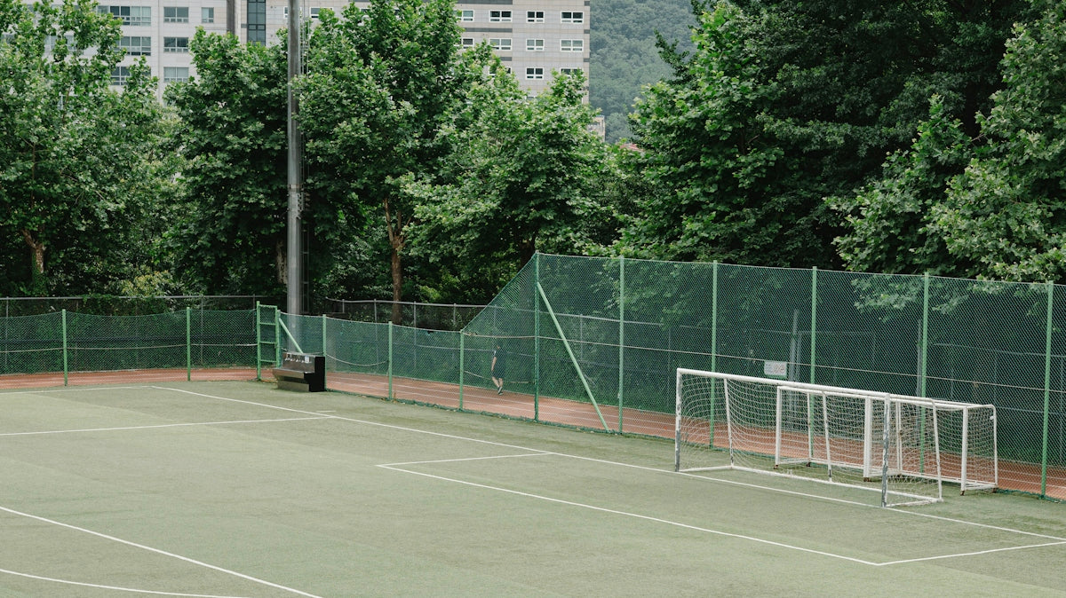 An empty sports field surrounded by green trees.