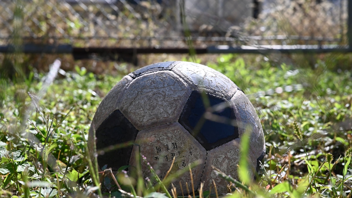 A worn soccer ball rests in overgrown grass.