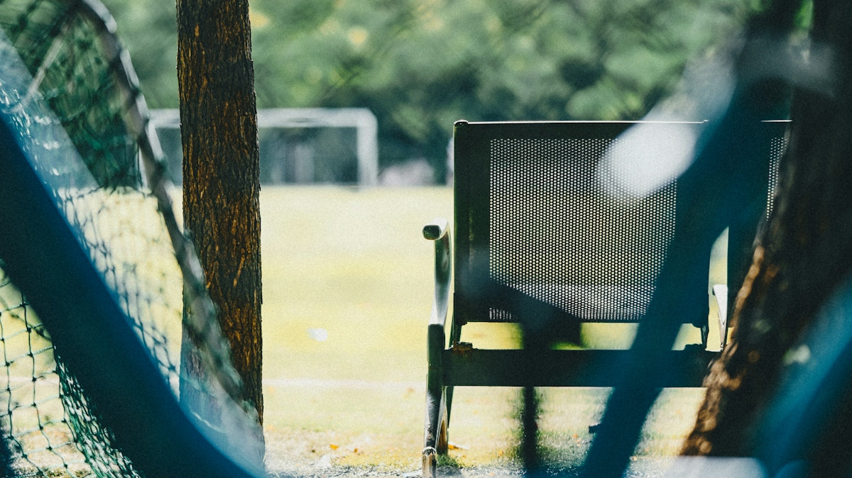 A metal chair facing a soccer field through a gap between two trees