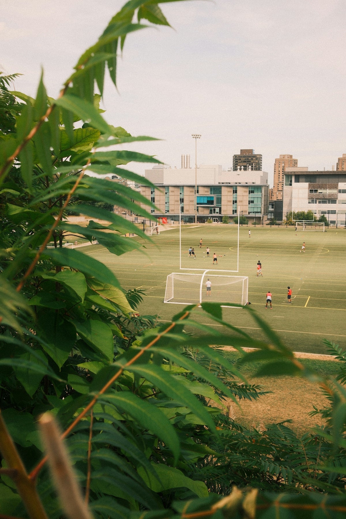 People playing soccer on a field with buildings behind.