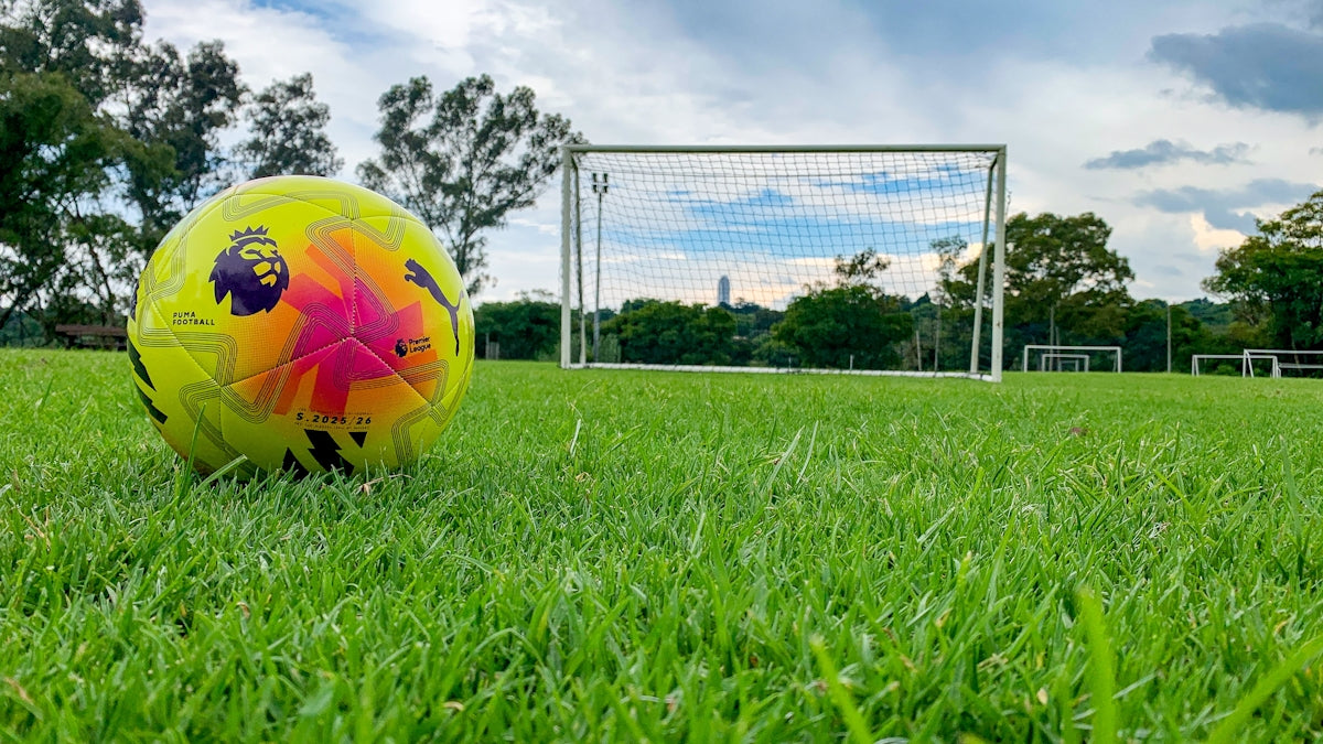 Soccer ball on green grass near a goal.