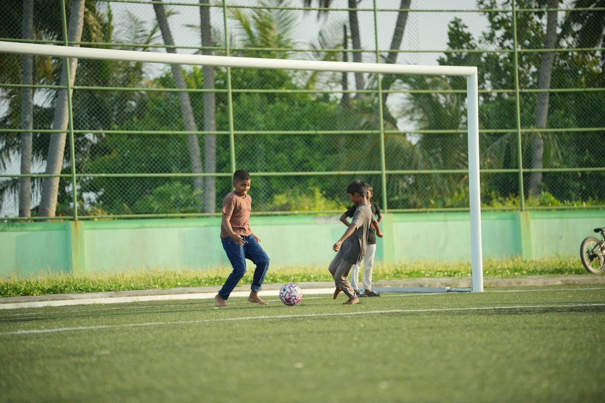 Three children playing soccer on an artificial turf field with a goal